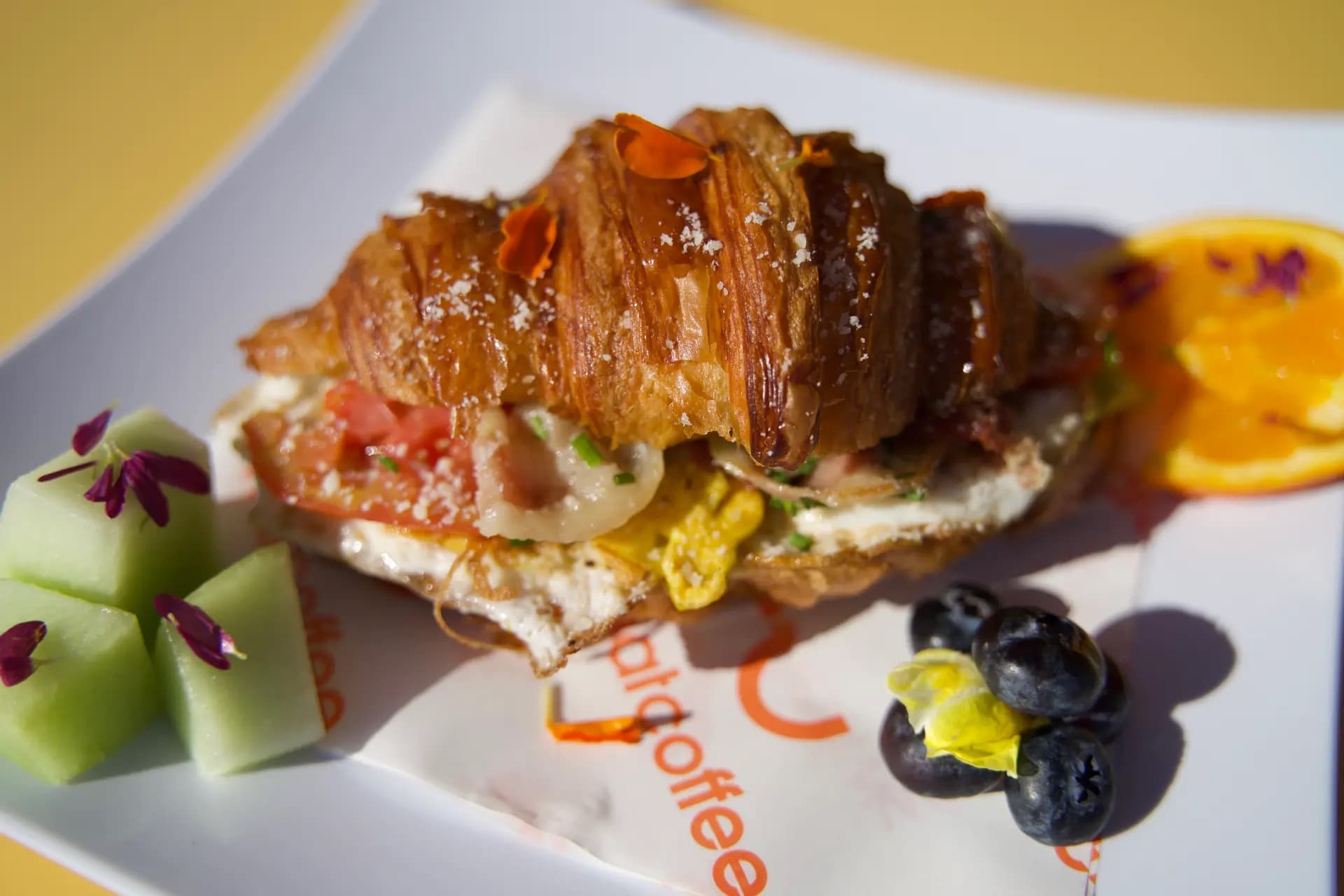Breakfast Sandwich - Bacon, egg, avocado and cheese on toasted croissant paired with a side salad and fresh seasonal fruits.